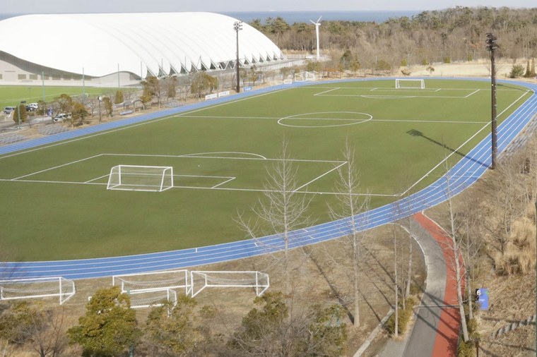 #PraCegoVer: Fotografia mostra um campo de futebol com uma pista de atletismo em volta. É o J-Village, local onde terá início o revezamento da tocha olímpica.