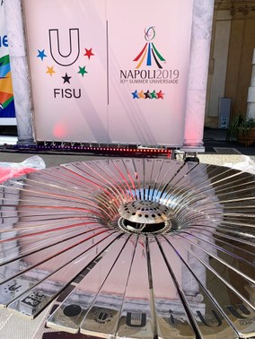 #PraCegoVer: A imagem mostra a logomarca e a tocha, ainda apagada, da Universíade 2019, maior competição universitária do mundo, que será disputada em Napoli, na Itália
